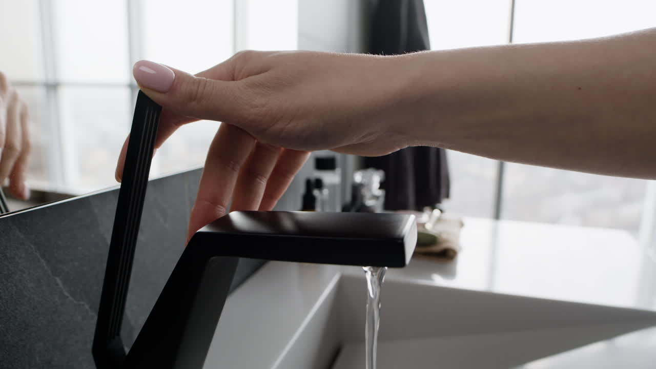 Woman turning on a modern black faucet