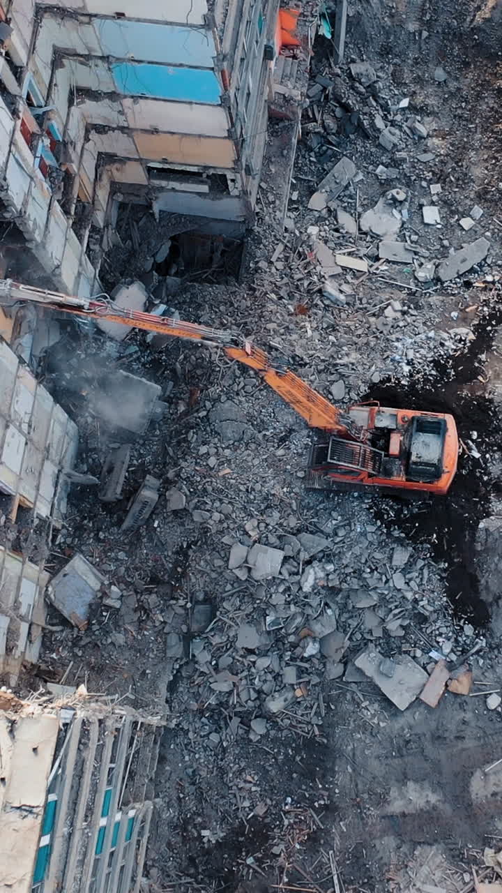 Tractor with a special bucket dismantles a collapsed building after a disaster. Construction work in the city. Shooting from the air. Vertical video