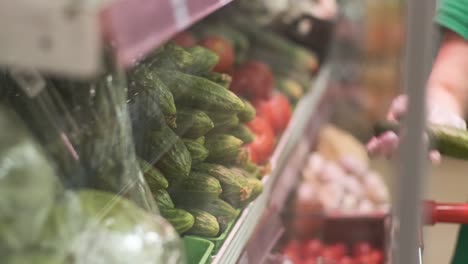 woman in rubber gloves picks fresh cucumbers and puts them in a plastic bag in a supermarket, close-up. coronavirus protection.