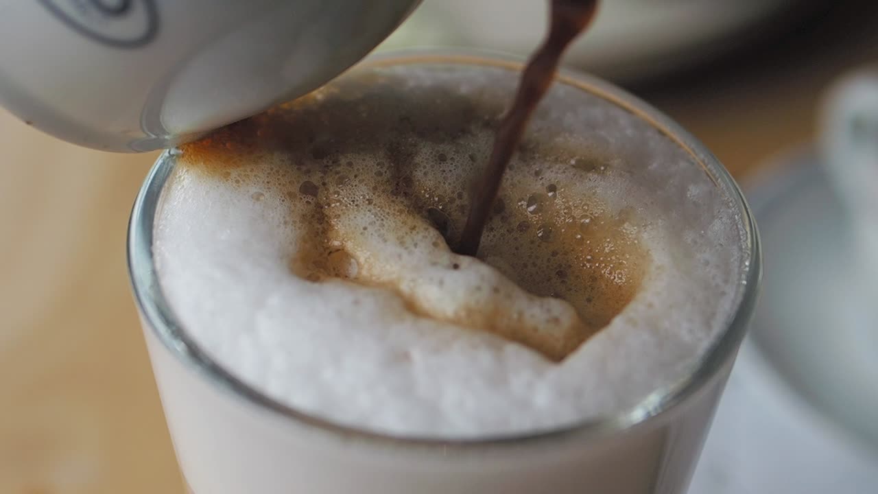라테 를 위해 에스프레소 를 우유 한 잔 에 부는 바리스타 의 클로즈업