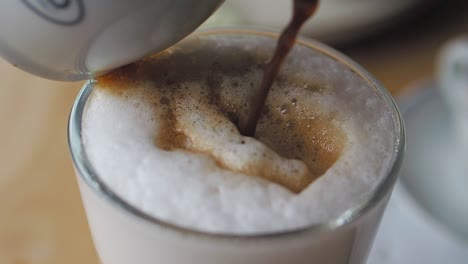 primer plano de un barista vertiendo espresso en un vaso de leche para un latte