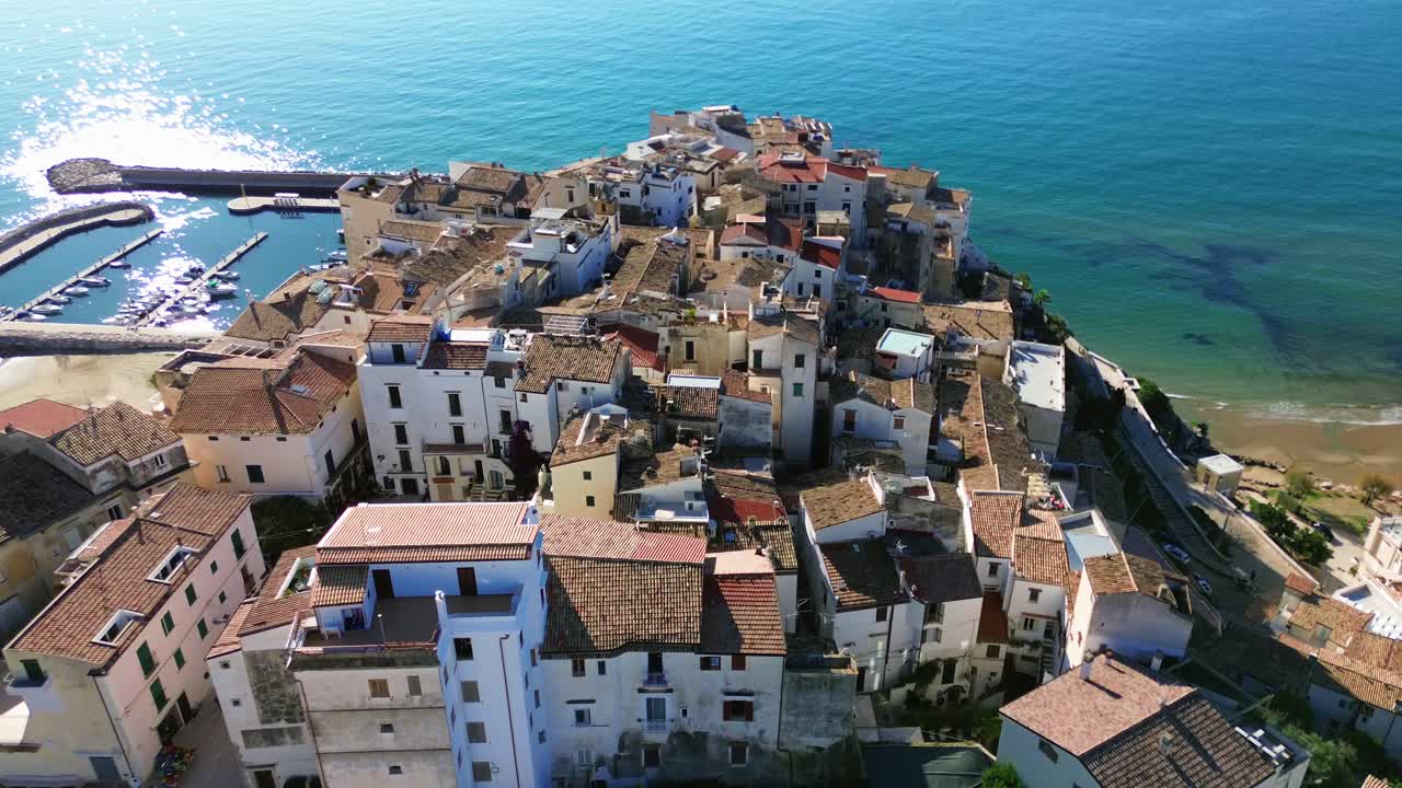 스페를롱가 언덕의 집들을 향해 공중으로 올라가며, 역사적인 매력과 반이는 물이 있는 아름다운 지중해 해안가를 강조합니다.