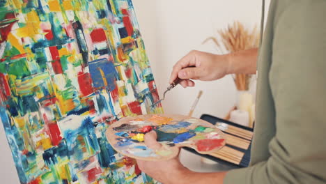 the hands of an unrecognizable man painting with a spatula on an impressionist canvas