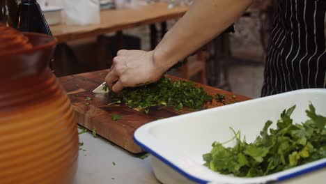 cierre las manos del chef cortando ensalada de hojas verdes en una tabla cortada de madera en una mesa de catering al aire libre