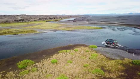 aerial over a black van driving through a river in the highlands of iceland