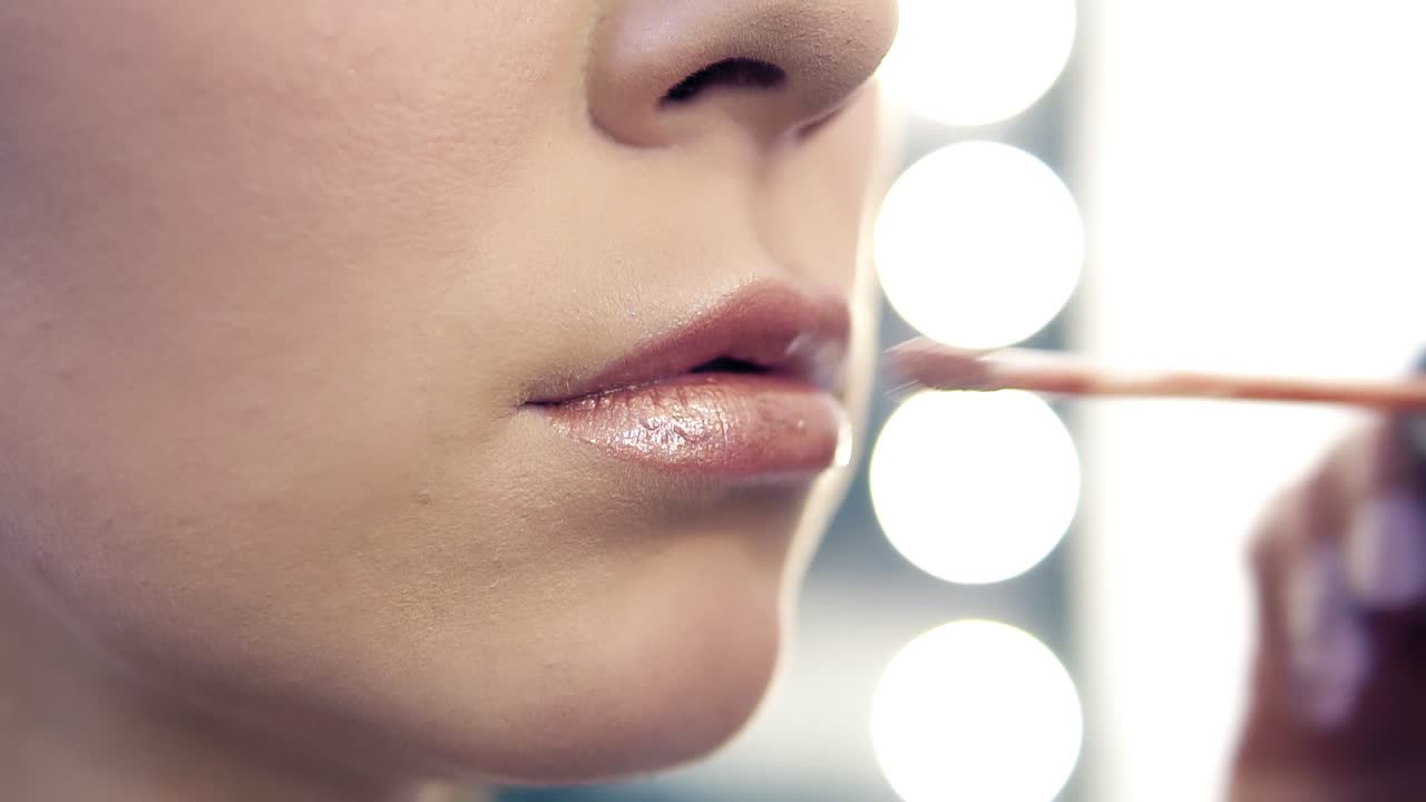 Closeup view of a professional makeup artist applying lipstick on model's lips working in beauty salon. Closeup view of an artist's hand using special brush