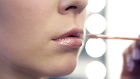 Closeup view of a professional makeup artist applying lipstick on model&#039;s lips working in beauty salon. Closeup view of an artist&#039;s hand using special brush