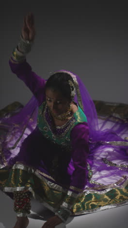 vertical video shot of female kathak dancer performing dance wearing traditional indian dress seated on floor in spotlight 1