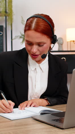 young businesswoman wears headset and takes notes during client video call on laptop smiling calmly