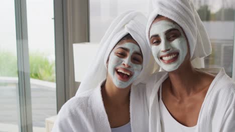 video of happy diverse female friends moisturizing with face masks in bathroom