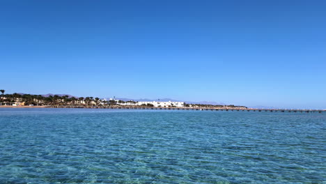 disparo aéreo de un dron volando sobre la superficie del mar con un muelle de madera visible en la distancia en un día soleado