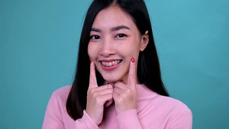 smiling asian woman wearing orthodontic retainer on blue screen background. dental care and healthy teeth.