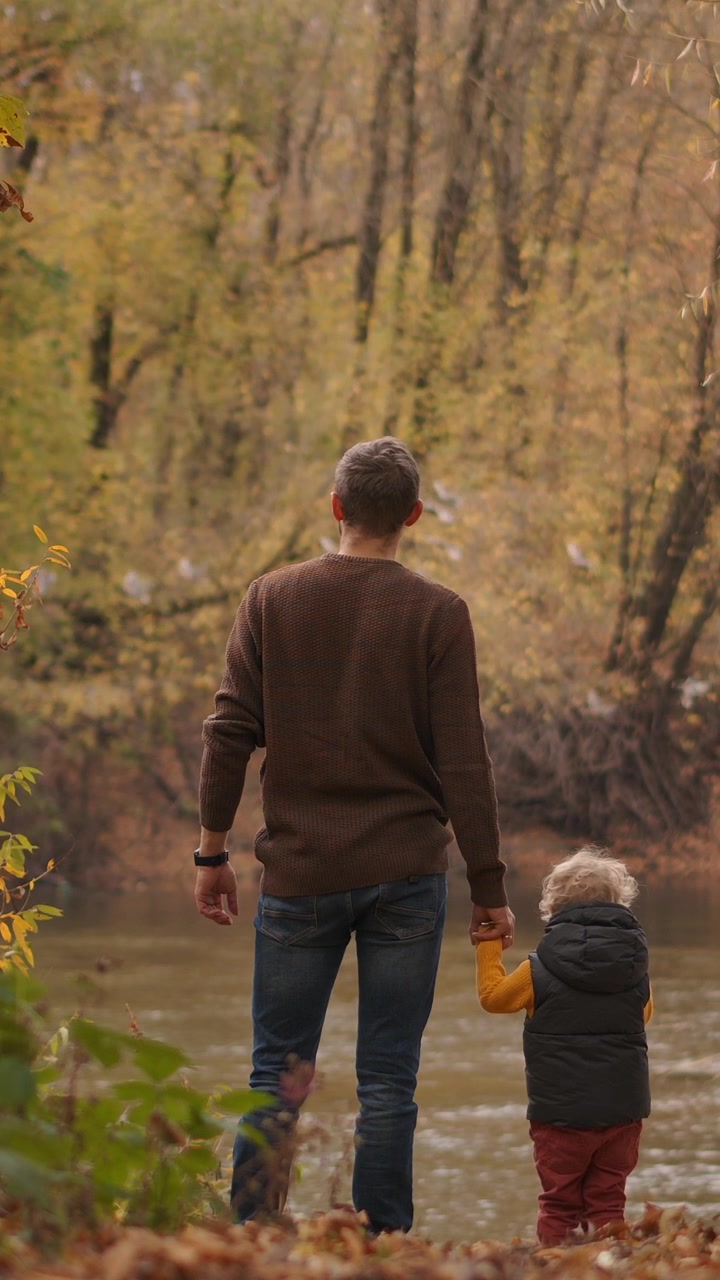 Padre e figlio che si tengono per mano in riva a un fiume in autunno