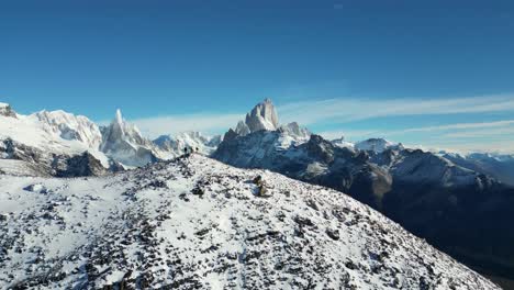 drone shot of hikers on a sow covered summit in patagonia, with the snow-covered peaks of fitz roy and cerro torre