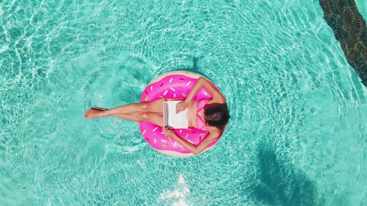 young woman swims in the sea in a swimming circle. Girl resting in the pool on an inflatable circle with a computer, top view