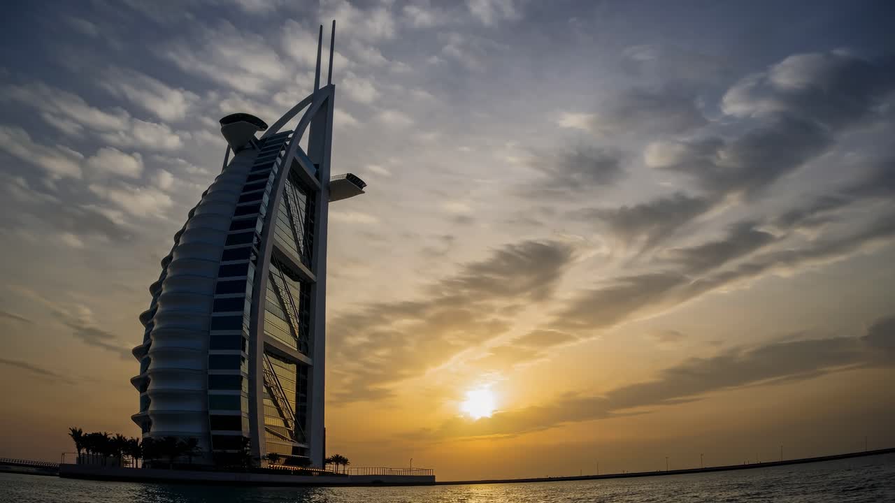 Majestic silhouette of Burj Al Arab Jumeirah against vibrant sunset sky, reflecting in calm waters of Persian Gulf, Dubai, UAE, showcasing iconic architecture and serene beauty