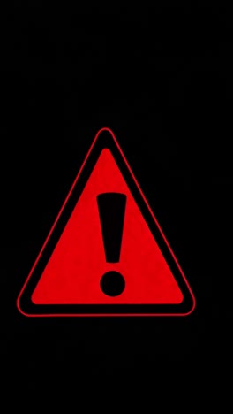 Close-up of a red warning triangle with an exclamation mark on a black background, shot