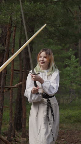 joyful teenage girls in elegant clothes fight on swords at summer camp quest slow motion. friends with ancient weapon. traditions of martial arts