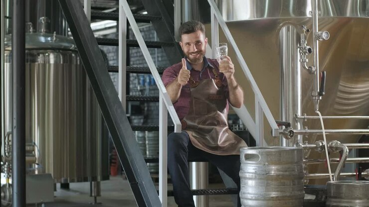 Young brewer wearing a leather apron is tasting beer at a modern brewery