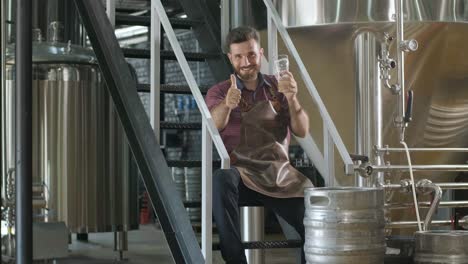 young brewer wearing a leather apron is tasting beer at a modern brewery