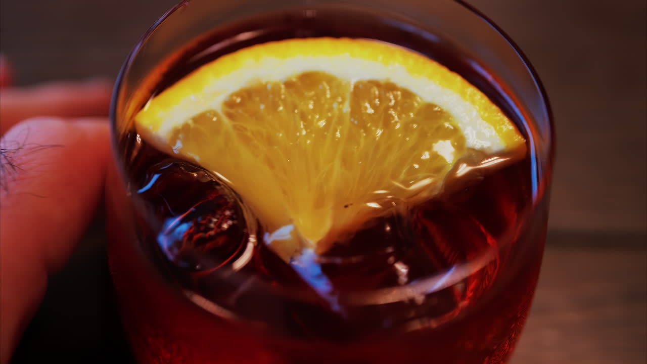 Primo piano di un cocktail Negroni con fetta d'arancia e cubetti di ghiaccio su un tavolo di legno