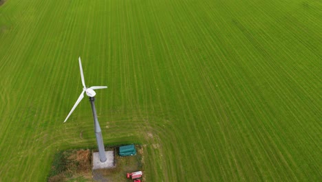 drone footage captures a single wind turbine spinning steadily above a lush, green agricultural field in kinross, scotland, under natural daylight