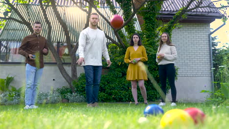 Front-view-of-caucasian-young-man-throwing-a-red-petanque-ball-in-the-park-on-a-sunny-day