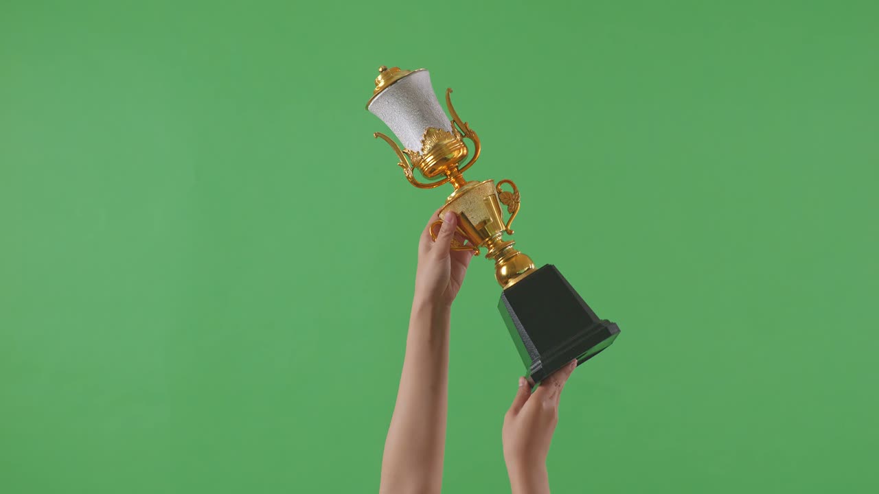 한 여성의 손이 트로피를 들고 있다. 녹색 화면 배경