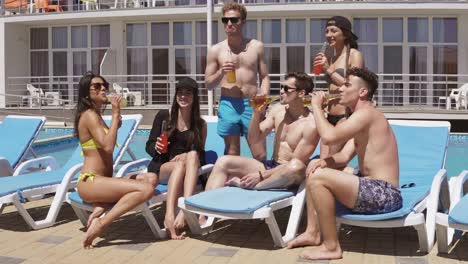 group of beautiful young friends drinking cocktails with cheers and having fun sitting by the swimming pool. shot in 4k