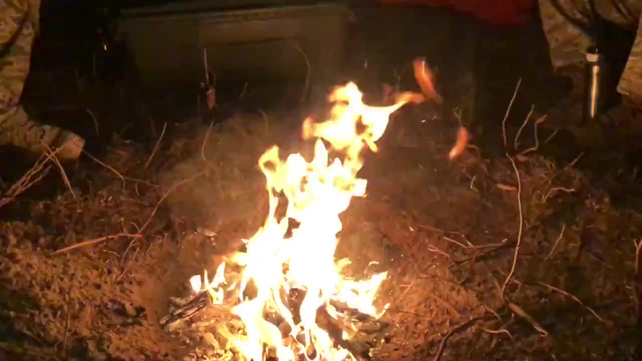 Large bonfire in the woods with some people's feet gathered around