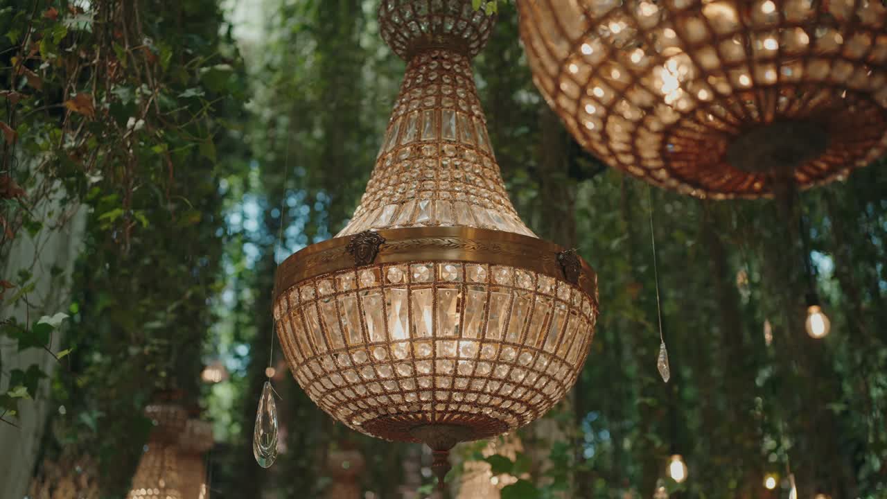 close up of ornate crystal chandelier surrounded by greenery in elegant outdoor event decor