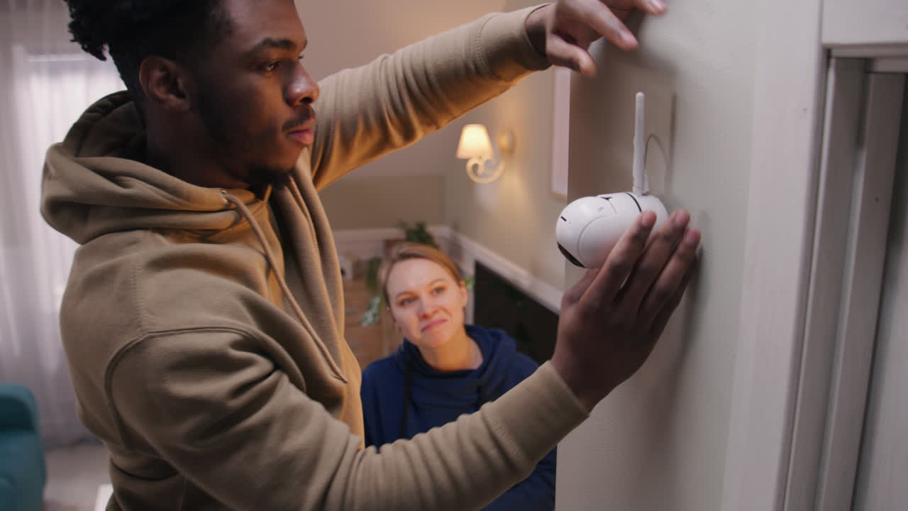 Man installing a wireless security camera at home with a woman present