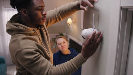 man installing a wireless security camera at home with a woman present