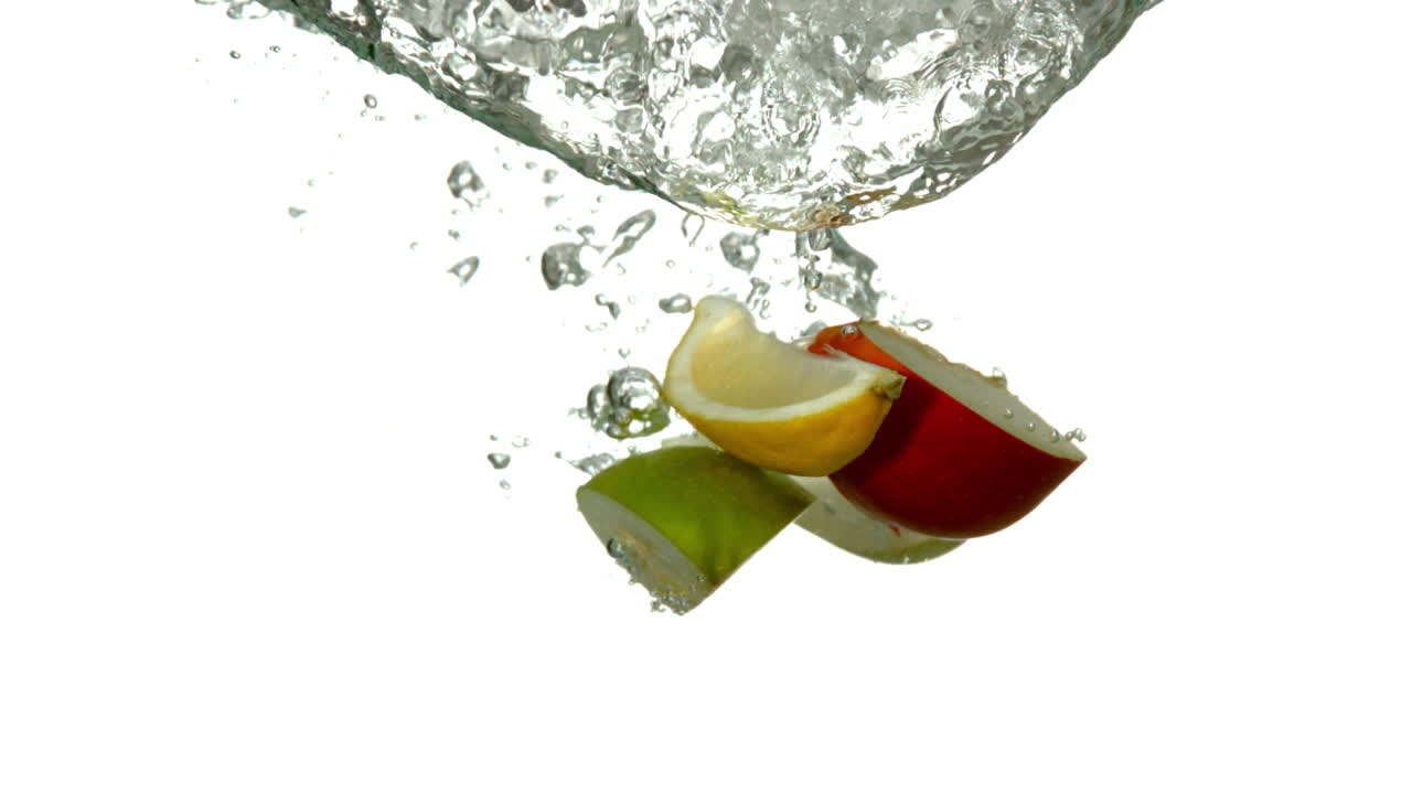 segmentos de frutas sumergiéndose en el agua sobre un fondo blanco