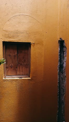 yellow building exterior with boarded window and plant