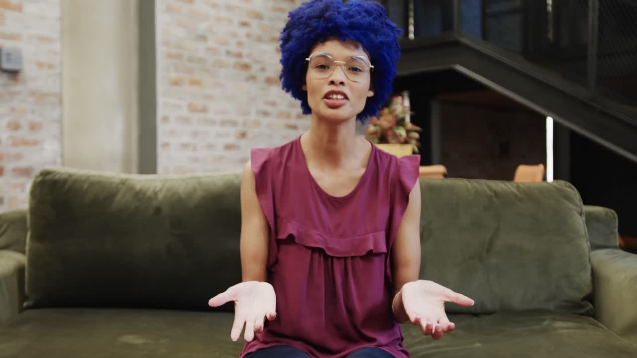 Empresária birracial feliz com afro azul fazendo videochamada no escritório, em movimento lento