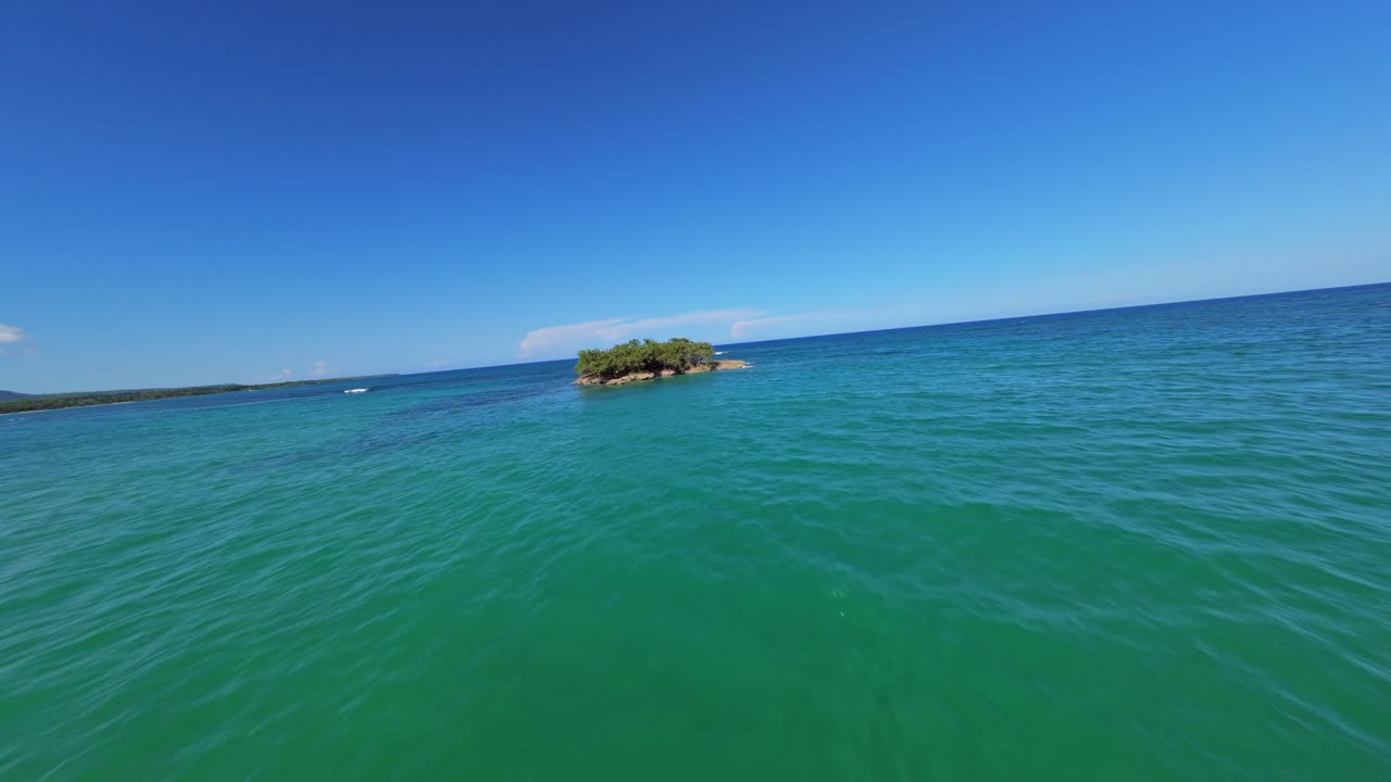FPV drone shot through palm tree forest and over a beach, toward a rocky isle