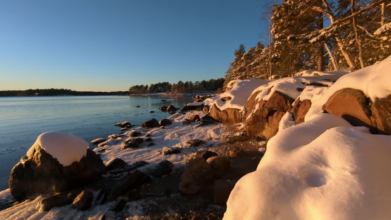 Rocky shore snowy beach by calm sea in winter