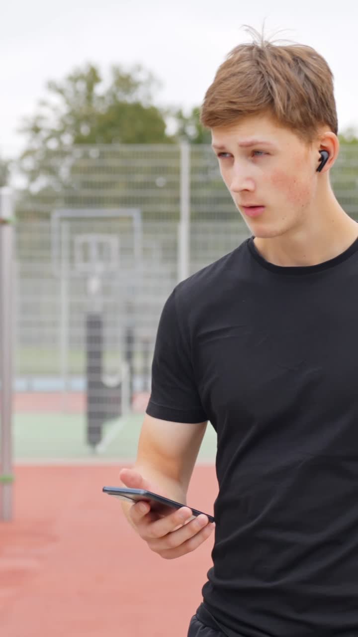 Man with wireless earbuds uses his smartphone before a workout, vertical