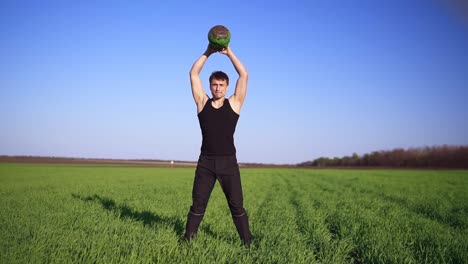 a strong man demonstrates an exercise with weight. lifting the bob with both hands. clear blue sky, green field. front footage