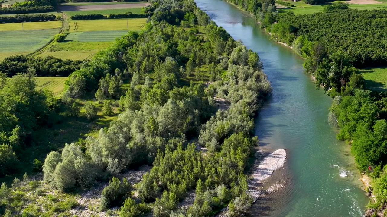 Letecký záběr dronem z vysokého úhlu zachycuje klikatou řeku podél svěžích zelených sadů a zemědělských polí.