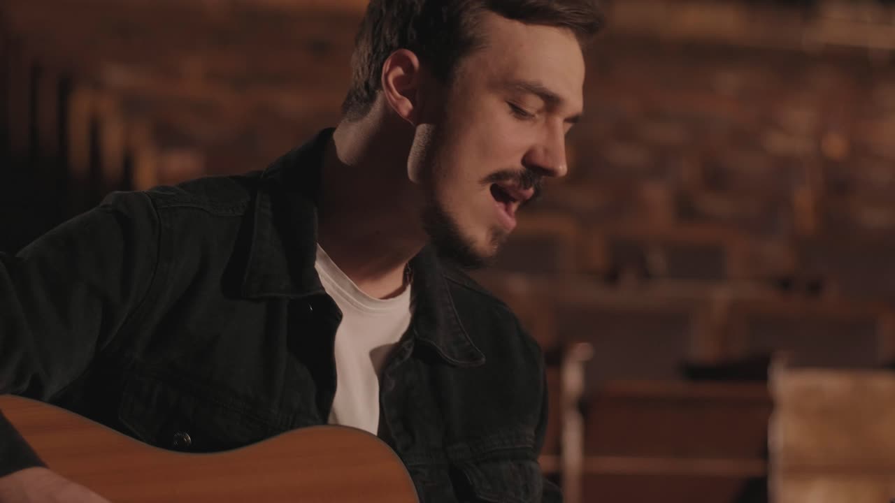 un chico guapo toca una guitarra acústica en un cine abandonado. el músico canta una canción y acompaña en la guitarra