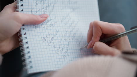 close-up of rear view of lady writing in notebook, focusing on hand holding pen and handwriting on grid paper. soft focus on hand as she writes with concentration