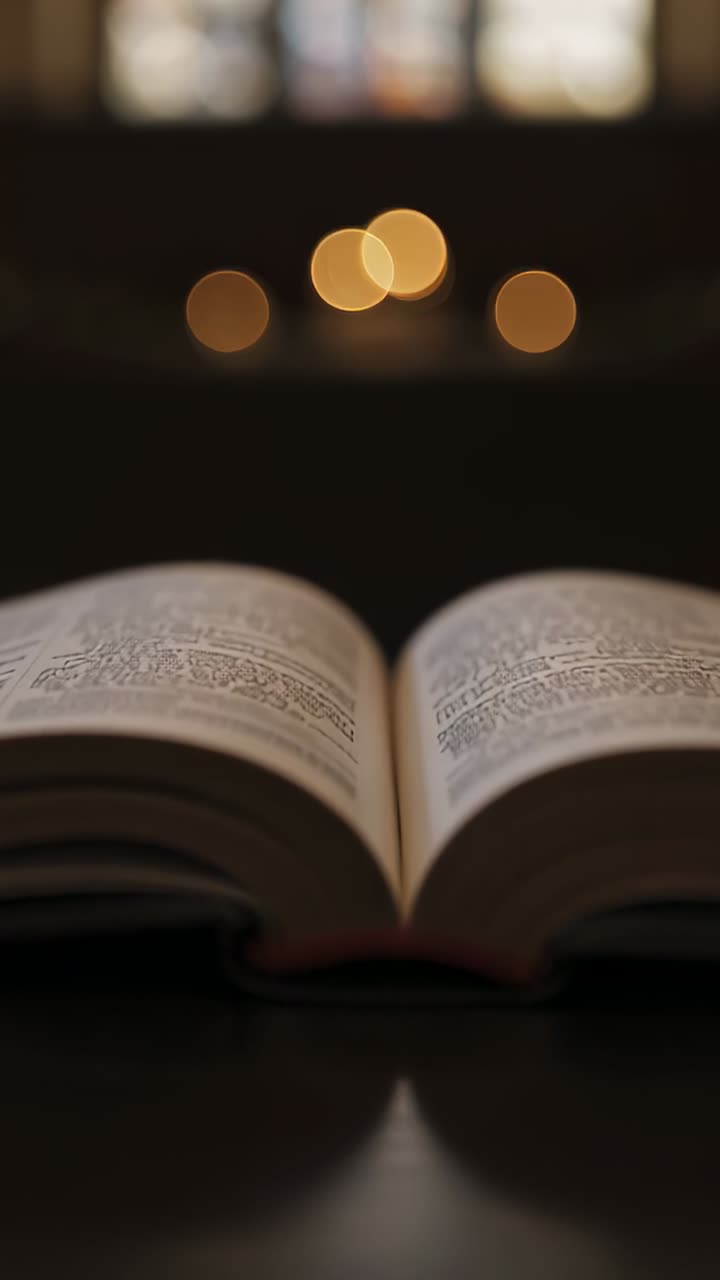 Vertical video: Camera filming open book resting on polished table, showing warm bokeh lights