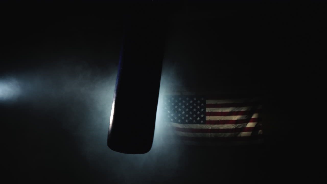 Un sacco da boxe ondeggia nella sala nella nebbia e sotto i riflettori sullo sfondo della bandiera statunitense, video 4K.