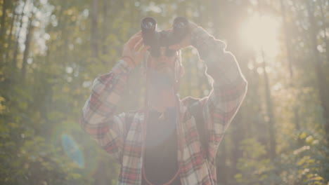 young man looking through binocular standing in forest