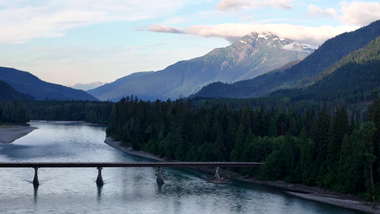 Aerial shot of a serene bridge spanning a river at Terrace, surrounded by lush green mountains under soft, diffused light.