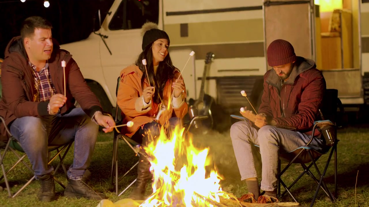 Amici arrostiscono marshmallow mentre si rilassano accanto al fuoco