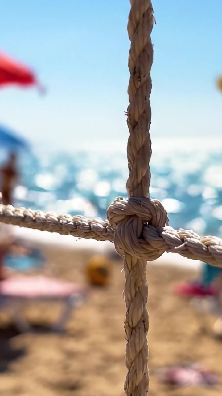 Primo piano su un nodo: una vista ravvicinata di una corda attorcigliata in un vivace ambiente da spiaggia con acqua illuminata dal sole e ombrelloni colorati sullo sfondo