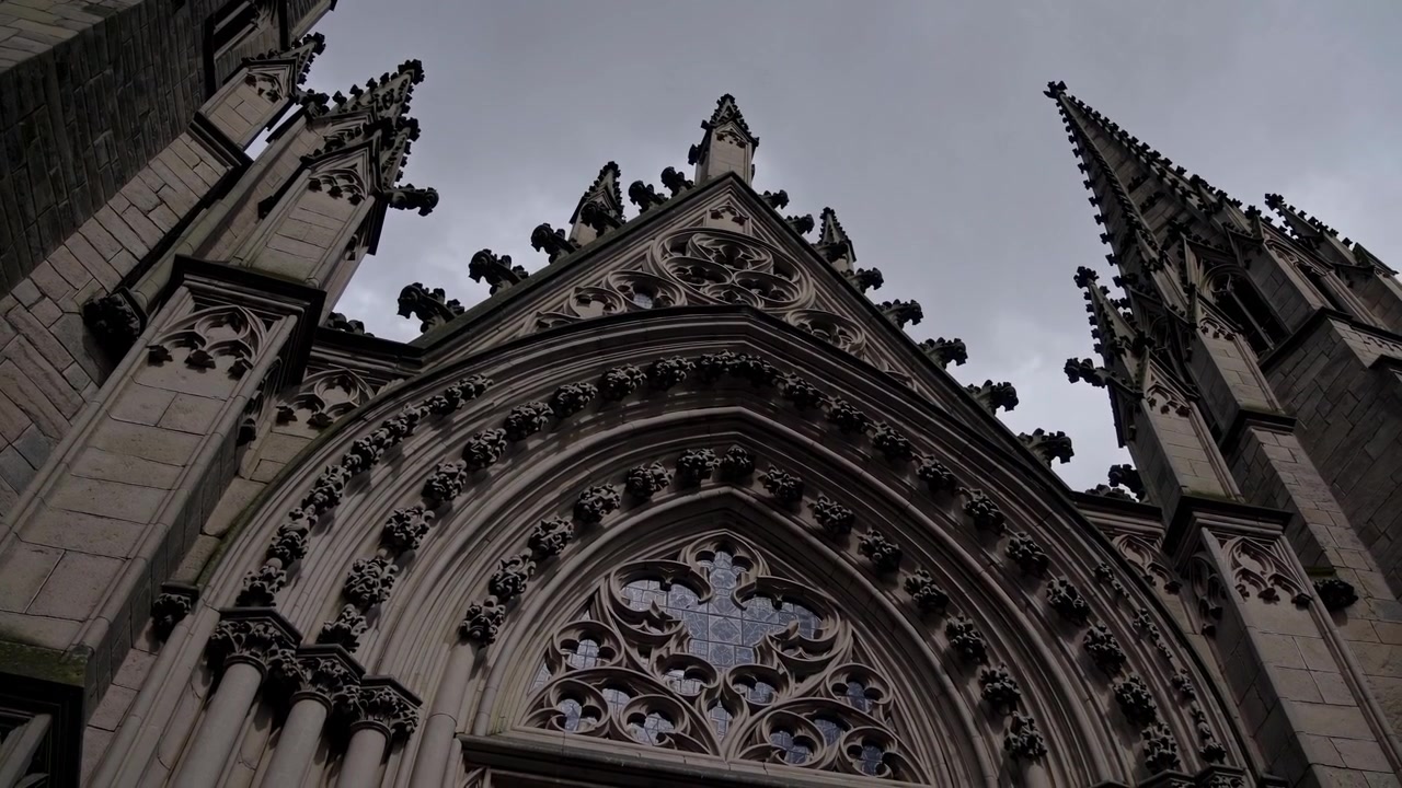 Untersicht einer verzierten gotischen Kirchenfassade vor einem grauen Himmel
